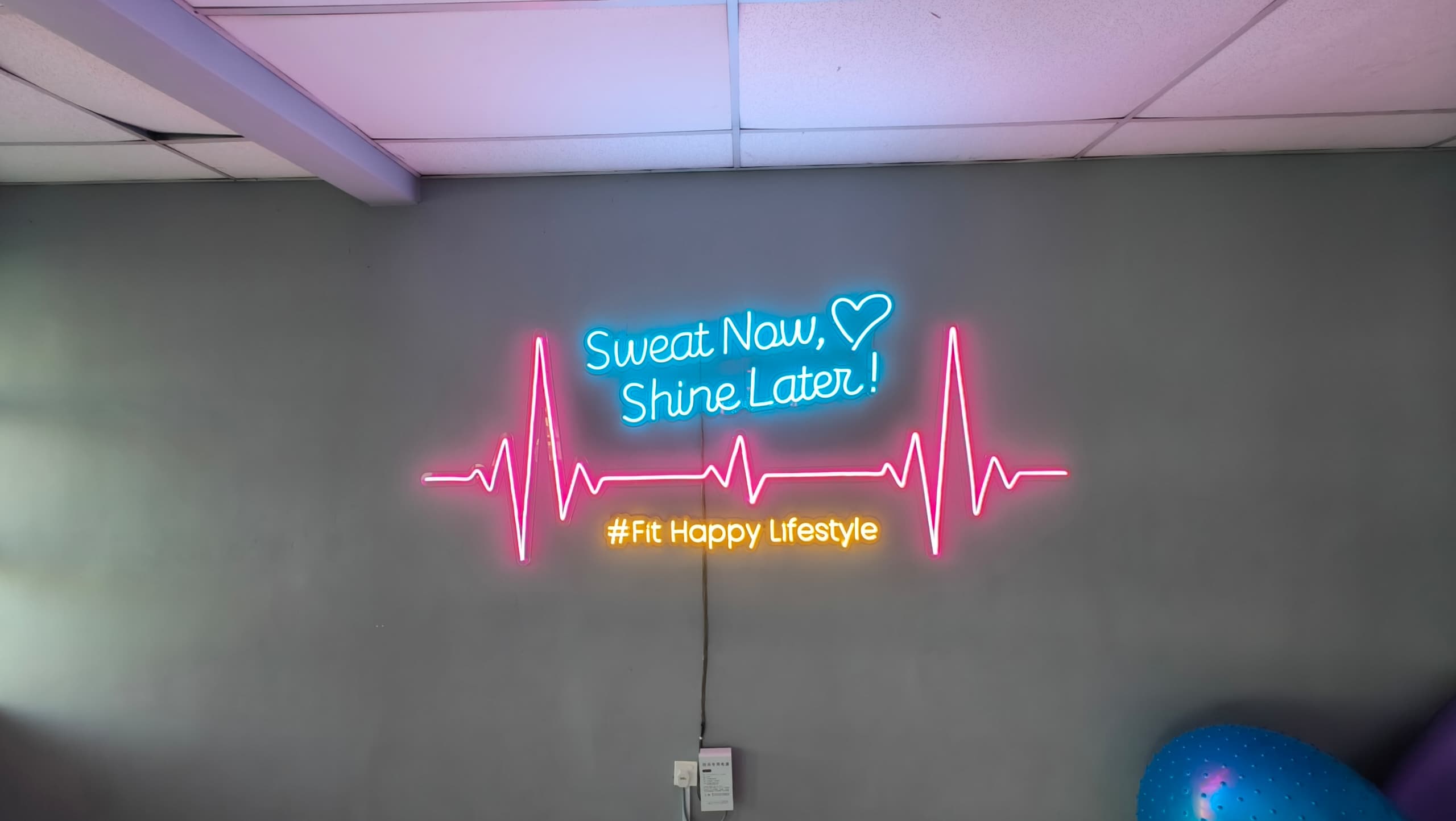 Sweat Now Shine Later neon motivational sign with heartbeat line and Fit Happy Lifestyle tagline at Meet In Studio